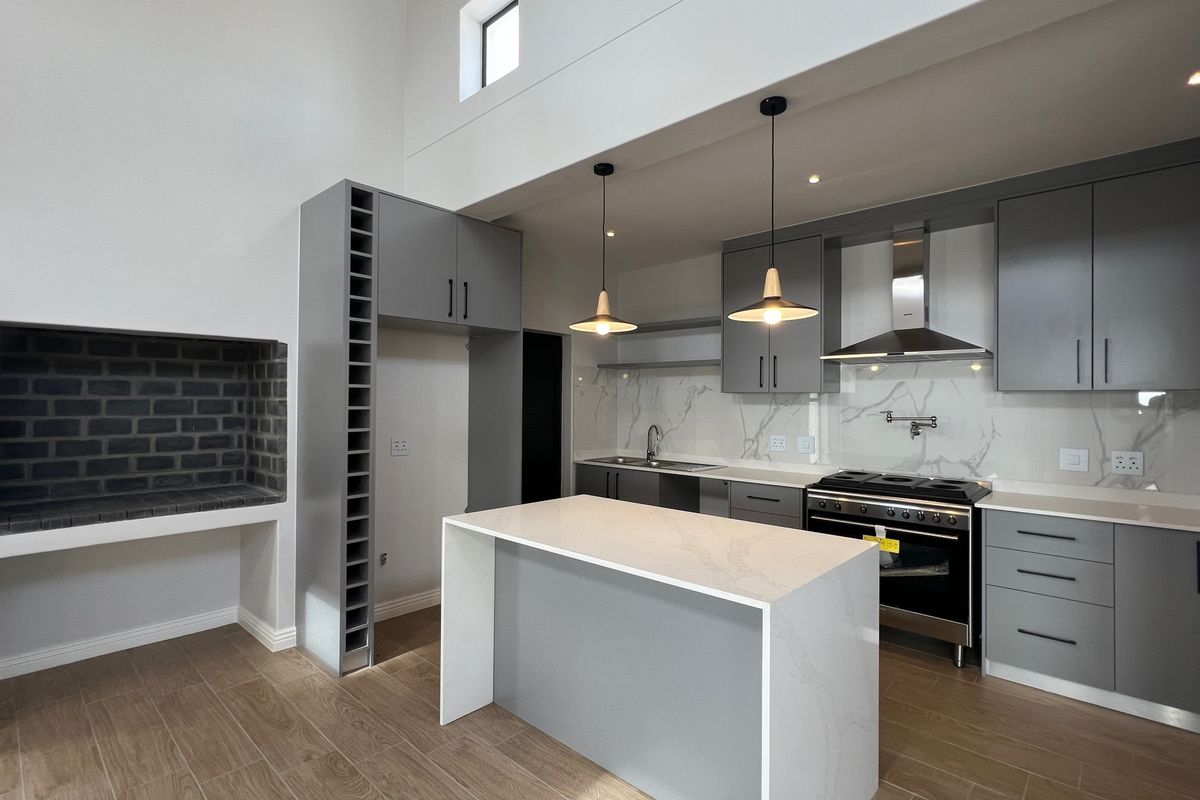 Modern open-plan kitchen featuring sleek grey cabinetry, stone countertops, a central island, built-in fireplace, and high-end stainless steel appliances.