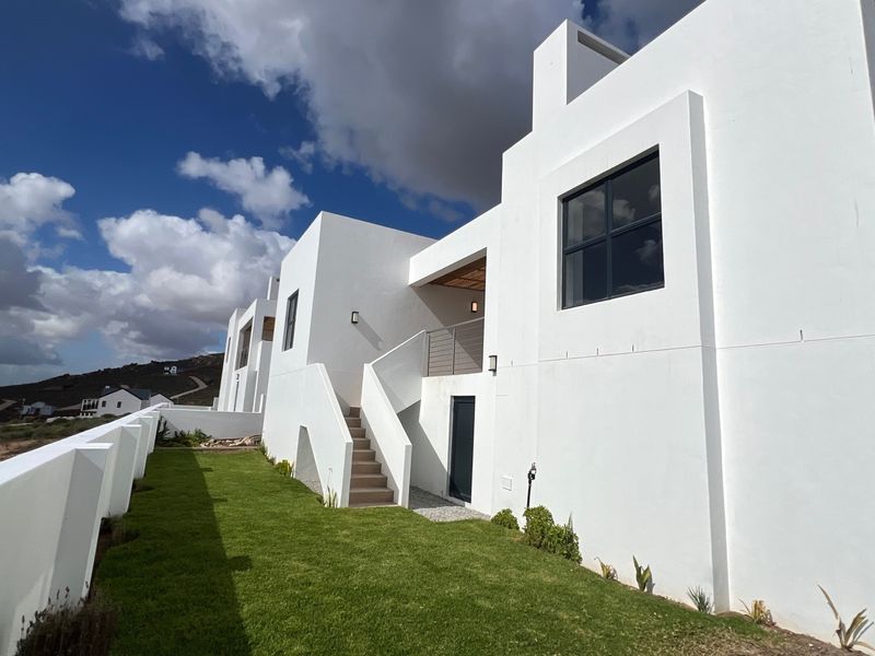 Modern white exterior rear facade featuring a clean architectural design, external staircase, balcony, and a well-maintained lawn area.
