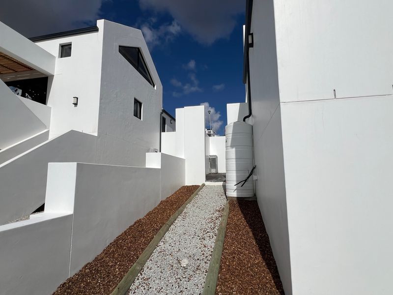 A clean, modern exterior side passage featuring white rendered walls, a gravel pathway with timber edging, and a functional water storage tank.