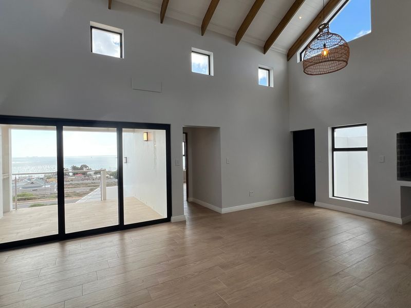 Spacious open-plan living area featuring vaulted ceilings with exposed timber rafters, large sliding doors leading to a balcony, and a built-in fireplace.