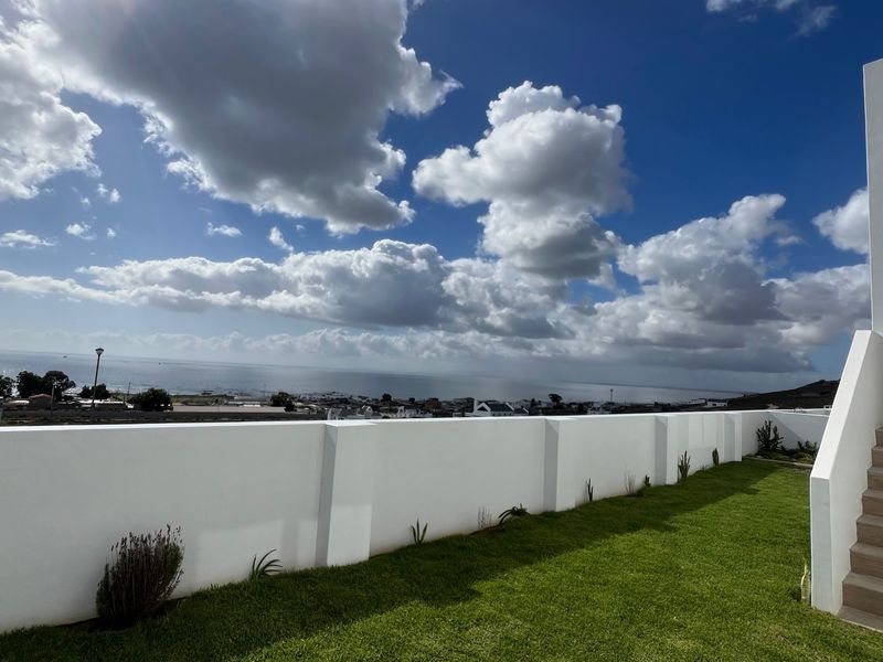A well-maintained rear garden area featuring a manicured lawn, a white retaining wall, and an external staircase with scenic coastal views.