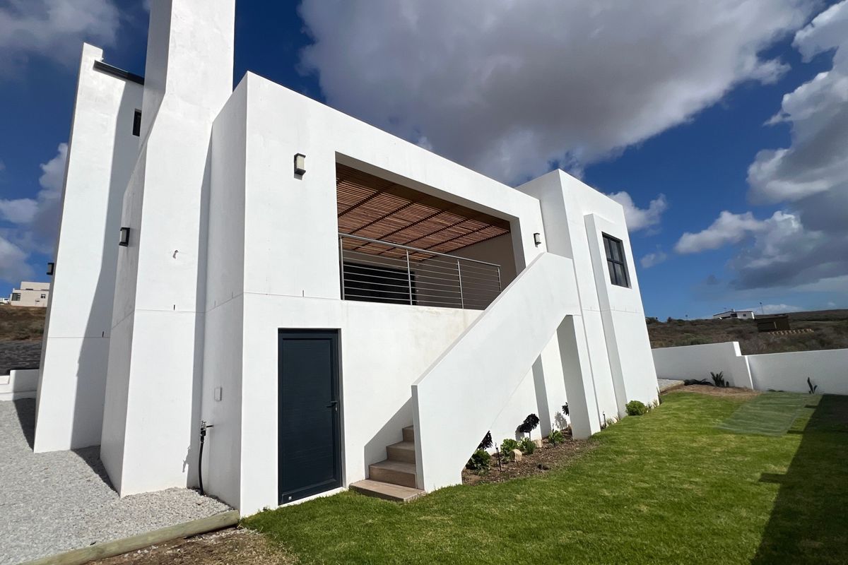 Rear view of a modern white house featuring a balcony with a timber pergola, external staircase, and a well-maintained lawn.