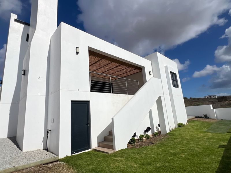 Rear view of a modern white house featuring a balcony with a timber pergola, external staircase, and a well-maintained lawn.