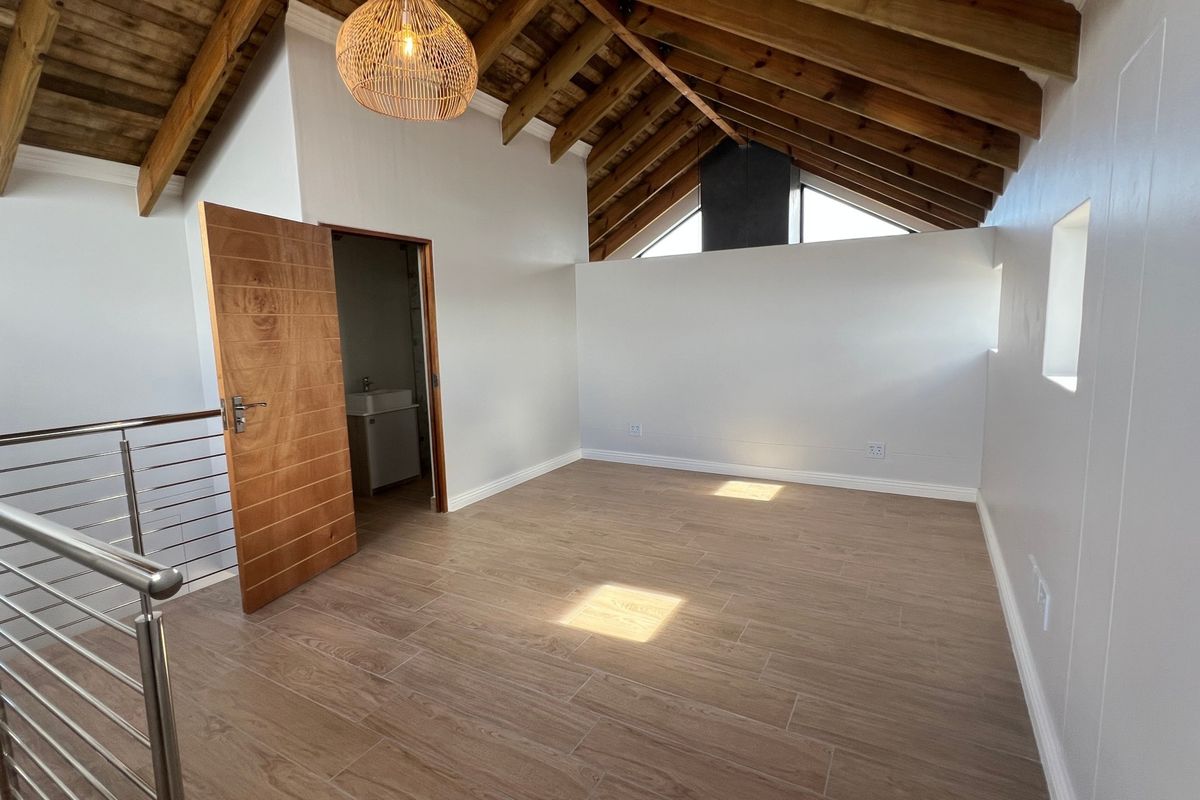 Spacious bedroom featuring high vaulted ceilings with exposed timber rafters, wood-look tiled flooring, and a modern stainless steel balustrade.