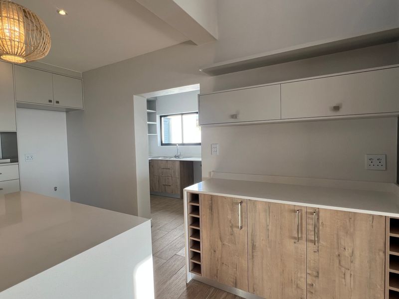 Modern kitchen featuring light wood-grain cabinetry, stone countertops, integrated wine storage, and tiled flooring, with an adjacent scullery area visible.