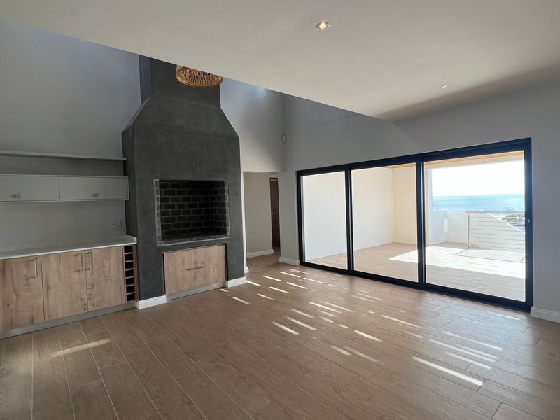 Spacious open-plan living area featuring a modern built-in fireplace, wood-look tile flooring, and large sliding doors opening to a balcony with ocean views.