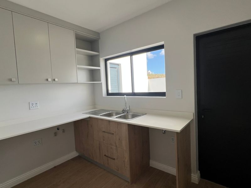 A clean, modern scullery featuring light-toned cabinetry, wood-finish base units, a stainless steel sink, and plumbing connections for laundry or kitchen appliances.