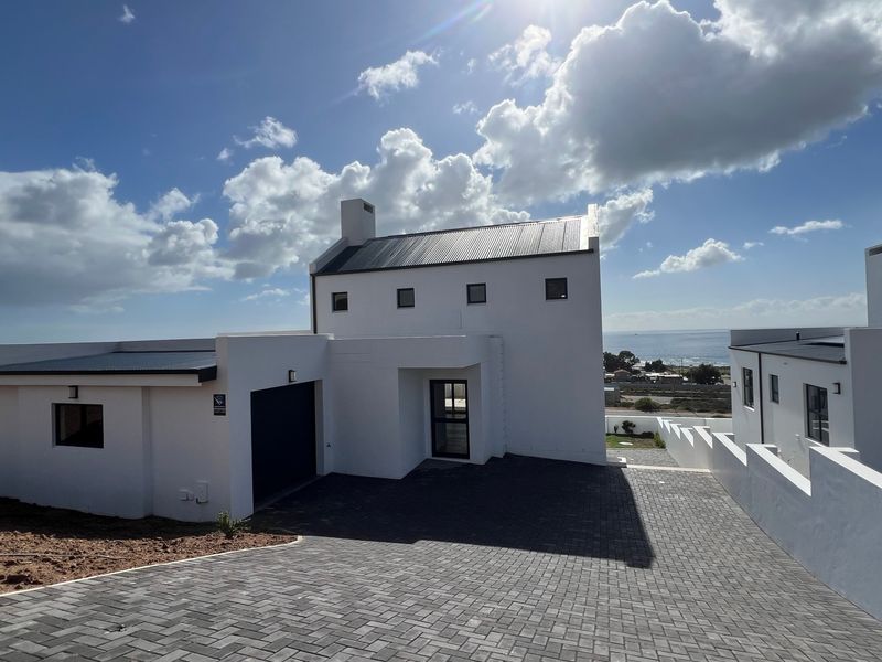 Modern white exterior facade with a paved driveway, metal roofing, and ocean views in a coastal residential setting.