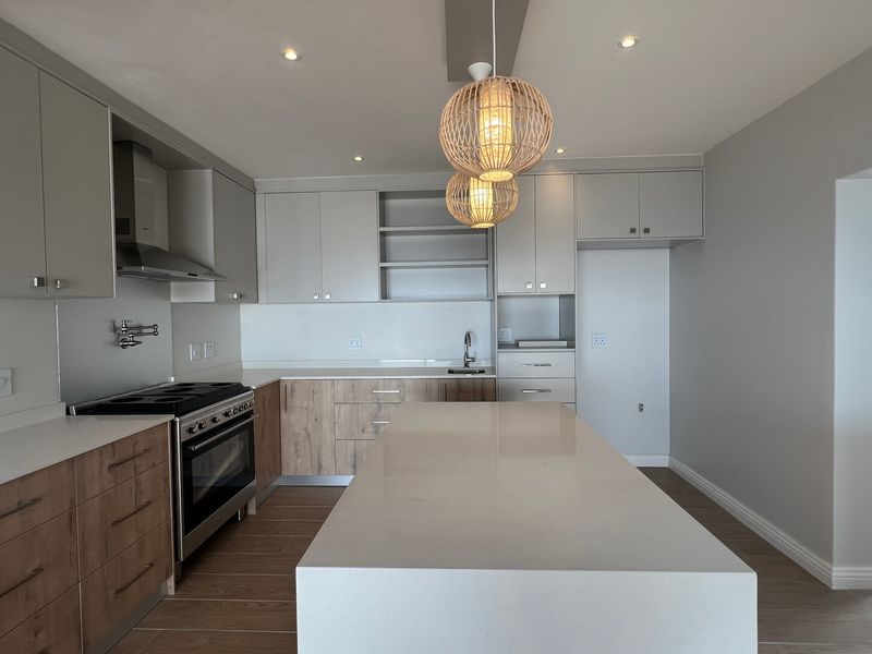 Modern kitchen featuring a large central island, quartz countertops, two-tone cabinetry, and high-quality stainless steel appliances in a bright, open-plan layout.