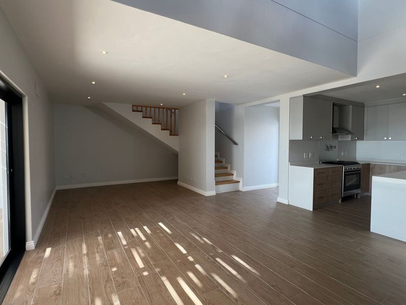 Spacious open-plan living area featuring modern kitchen with island, timber staircase, and large sliding doors leading to an outdoor space.