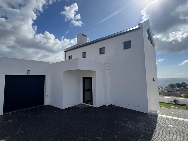 Modern white architectural home featuring a paved driveway, integrated garage, and clean lines with a coastal view.
