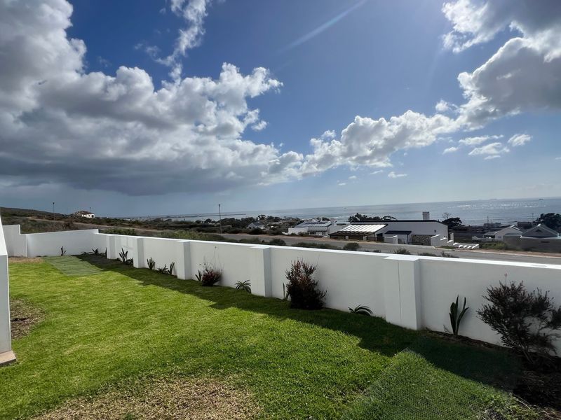 A well-maintained rear garden area featuring a crisp white boundary wall, manicured lawn, and an external staircase with scenic coastal views.