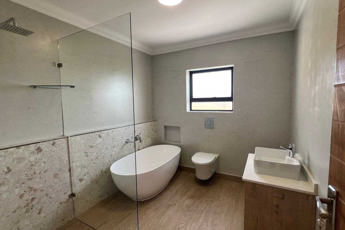 Modern bathroom featuring a freestanding bathtub, glass-enclosed shower, wall-hung toilet, and a vanity with a vessel sink, finished with contemporary terrazzo and wood-look tiles.