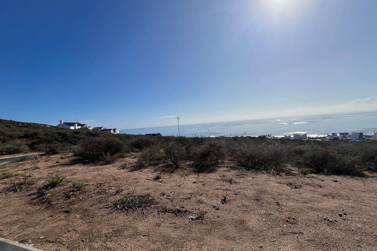 A wide-angle view of a vacant residential plot featuring natural coastal vegetation and expansive ocean views.