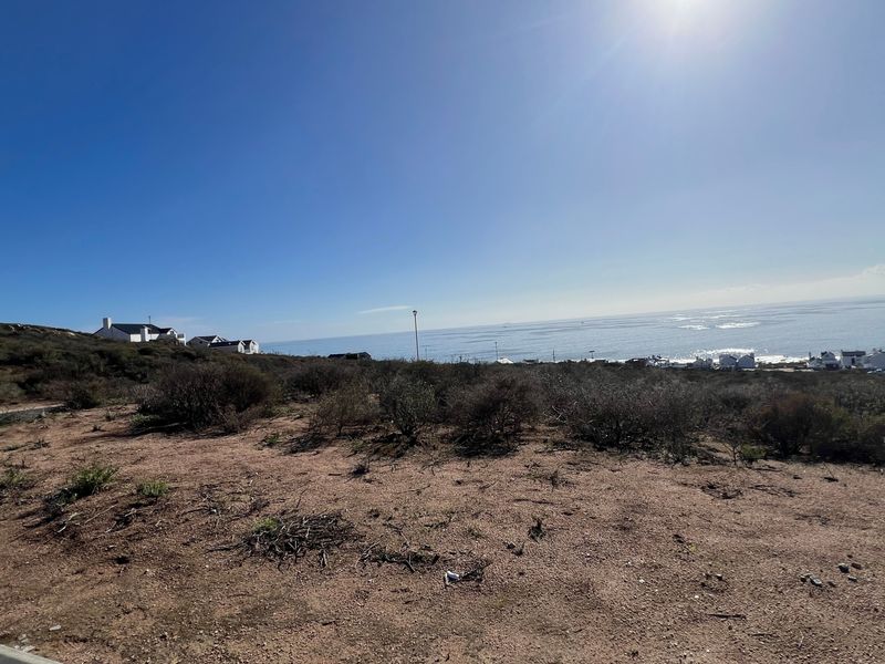 A wide-angle view of a vacant residential plot featuring natural coastal vegetation and expansive ocean views.