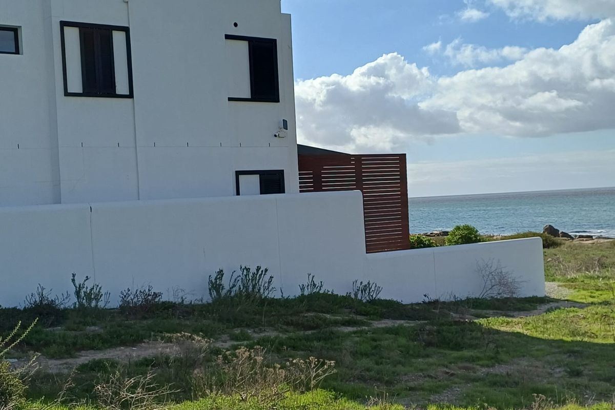 Rear view of the property featuring a white boundary wall, timber privacy screen, and direct proximity to the coastline.