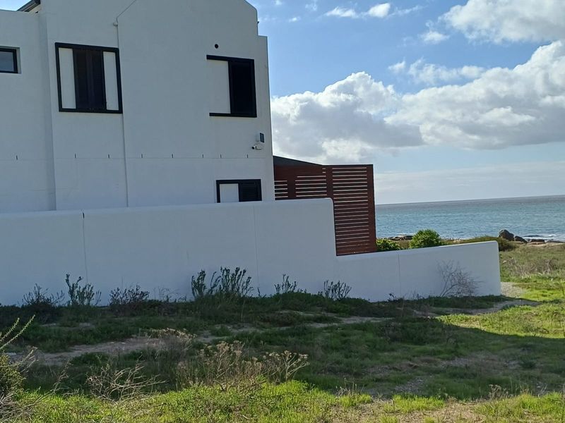 Rear view of the property featuring a white boundary wall, timber privacy screen, and direct proximity to the coastline.