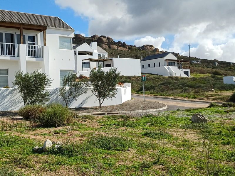 A view of the residential street frontage showing modern white multi-story homes with balconies and paved access roads in a coastal estate setting.