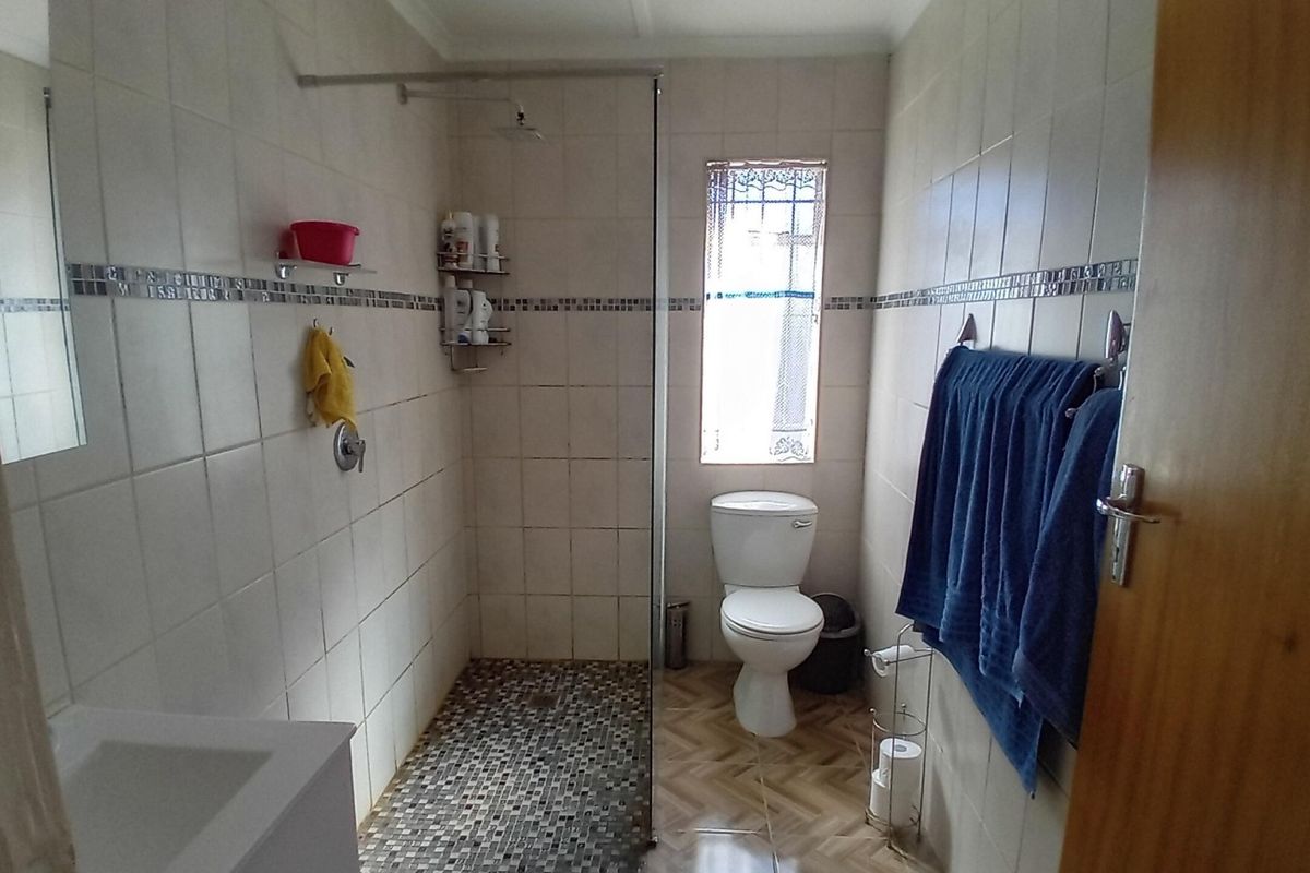 A functional bathroom featuring a walk-in shower with a glass screen, mosaic floor tiling, and neutral wall tiles.