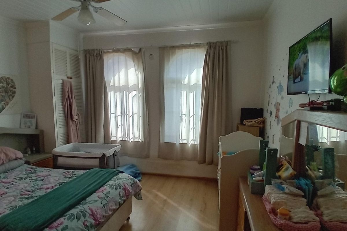 A functional bedroom featuring laminate flooring, built-in cupboards, and a ceiling fan, offering a comfortable and practical living space.