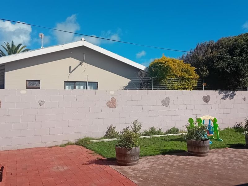 A rear exterior view featuring a concrete block boundary wall with electric fencing, a paved patio area, and a small lawn.