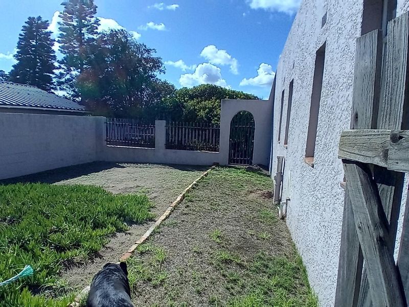 A rear exterior view of the property featuring a boundary wall, metal security gate, and a side yard area with basic landscaping.