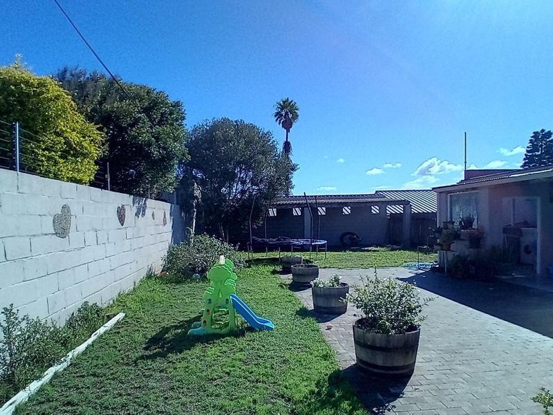 A rear garden area featuring a paved patio, lawn, and perimeter wall with electric fencing.