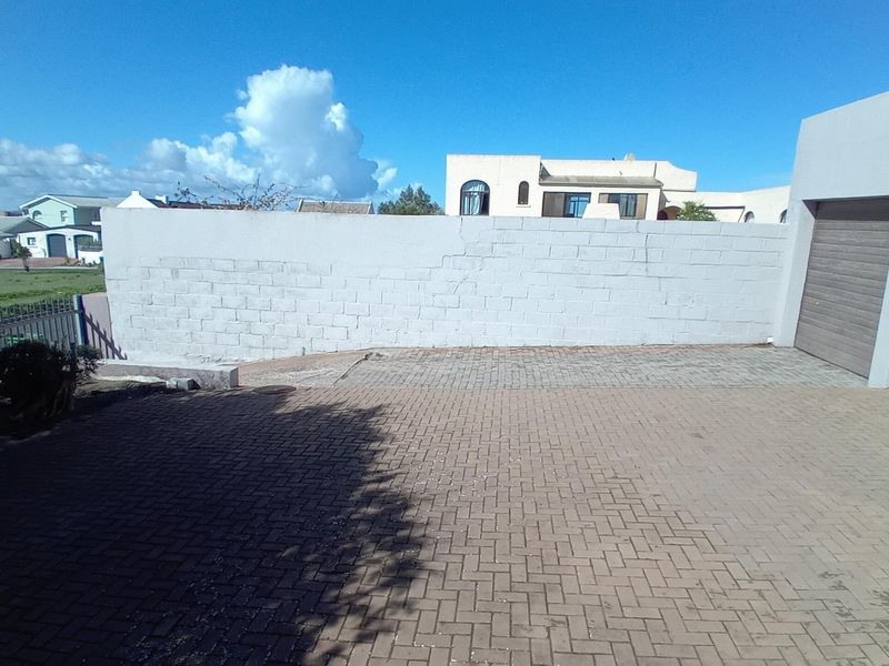 Front exterior view showing a paved driveway, a boundary wall, and access to the garage and pedestrian entrance.