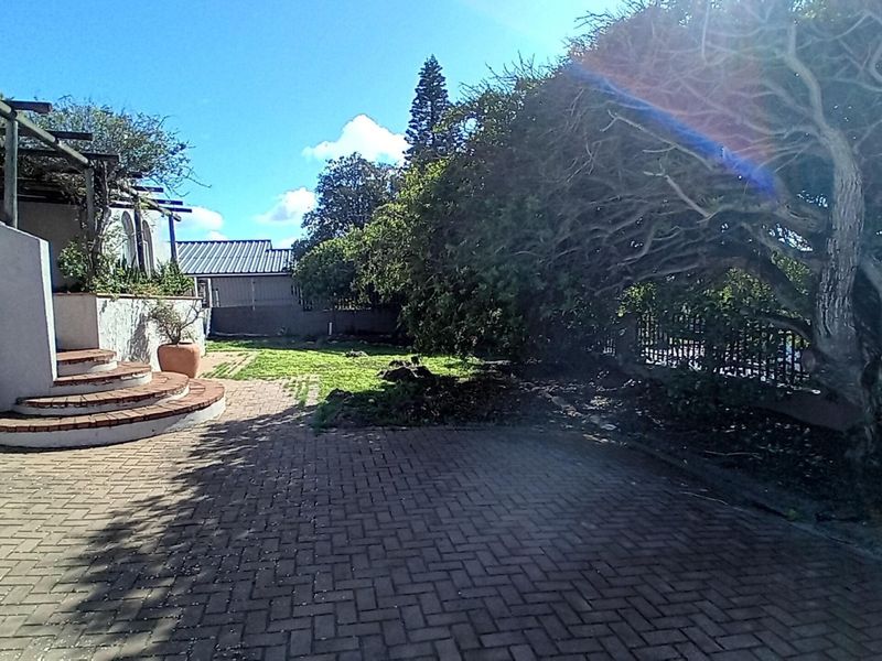 A rear garden area featuring a paved patio, a pergola structure, and brick steps leading to the house exterior.