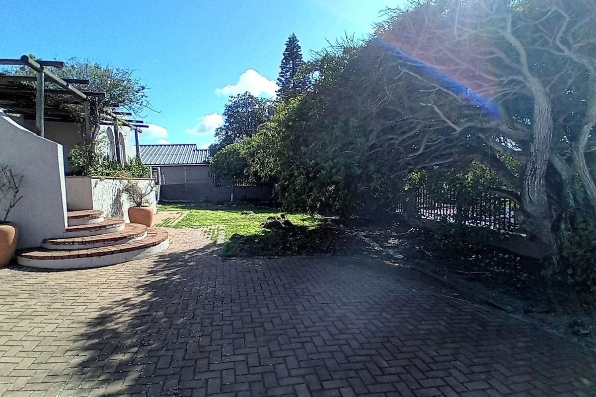 A rear garden area featuring a paved patio, a pergola structure, and brick steps leading to the house exterior.