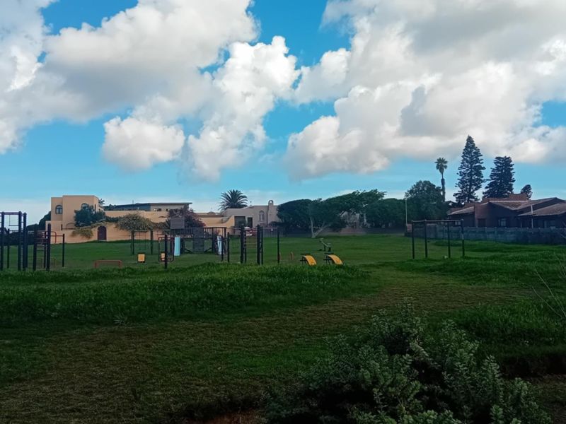 A communal outdoor area featuring playground and fitness equipment set within a large, open grassed space.