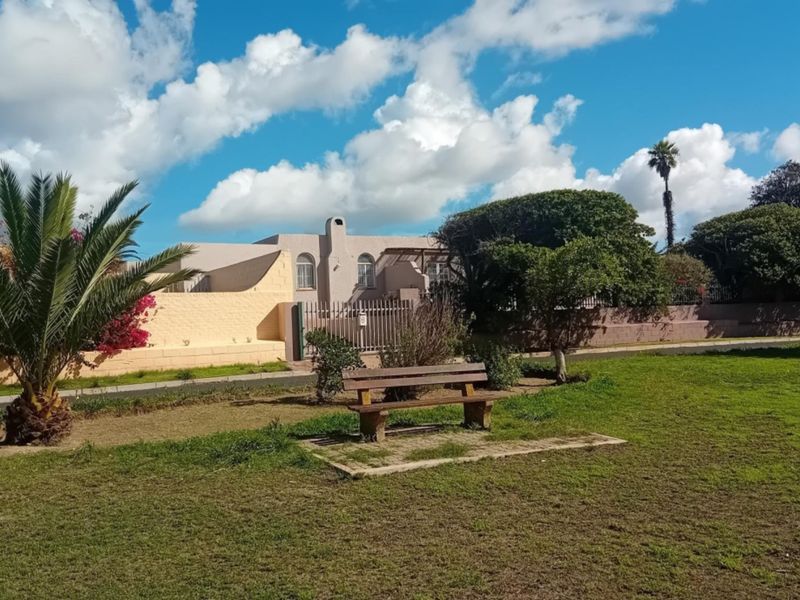 A view of the property's front exterior, featuring a landscaped garden, boundary wall, and gated entrance.