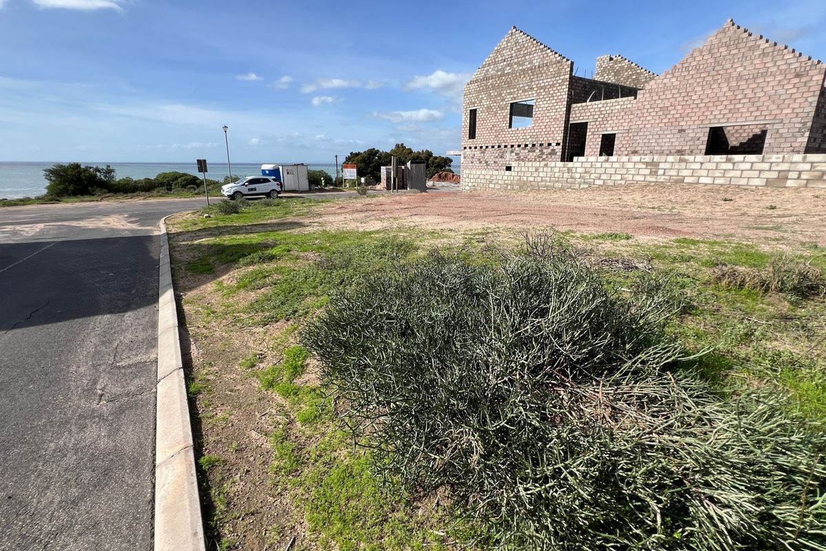 A vacant residential plot featuring an uncompleted masonry structure with ocean views, situated along a paved street.