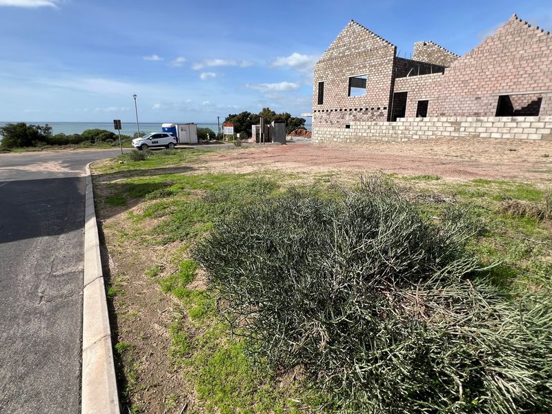 A vacant residential plot featuring an uncompleted masonry structure with ocean views, situated along a paved street.