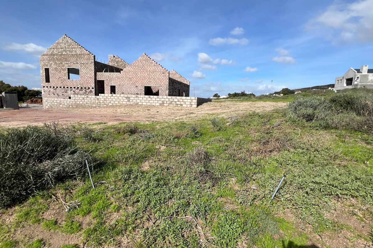 A vacant residential plot featuring an unfinished masonry block structure under construction, set within a natural landscape.