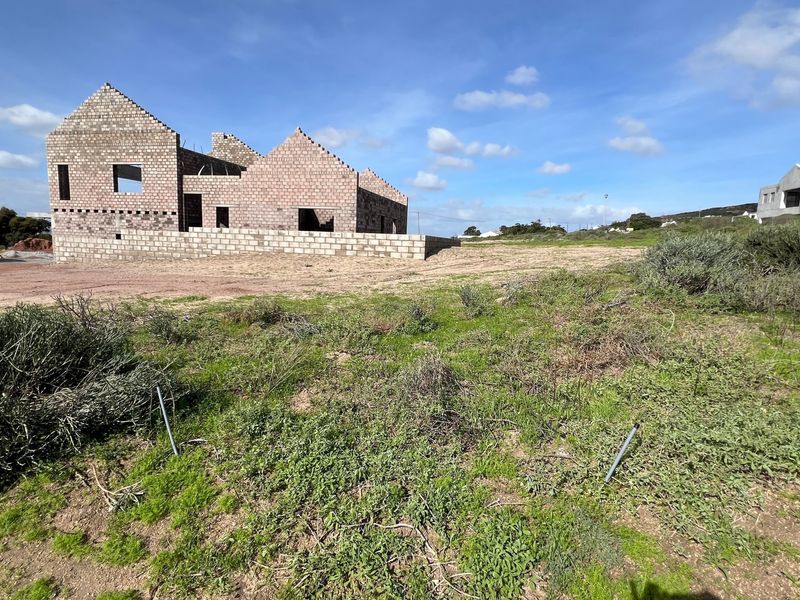 A vacant residential plot featuring an unfinished masonry block structure under construction, set within a natural landscape.