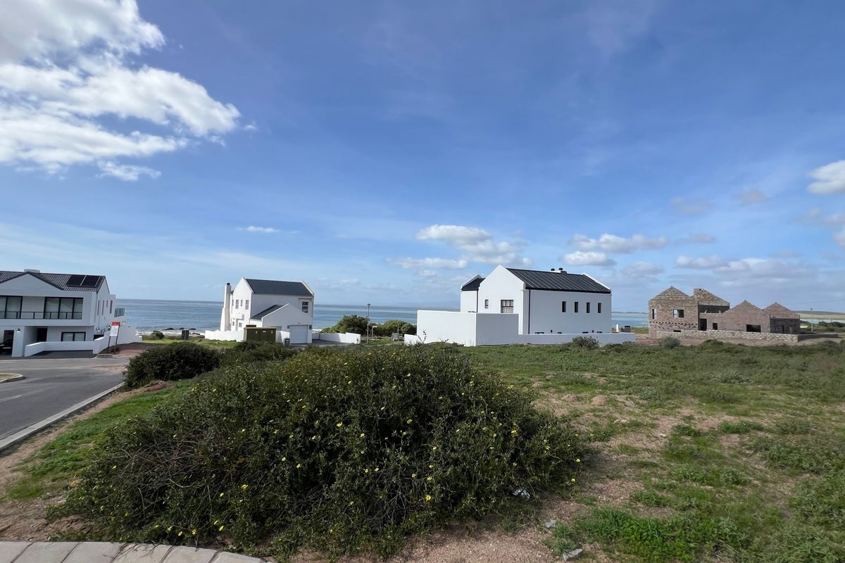 A wide-angle view of a coastal residential area featuring established homes and vacant land under a clear blue sky.
