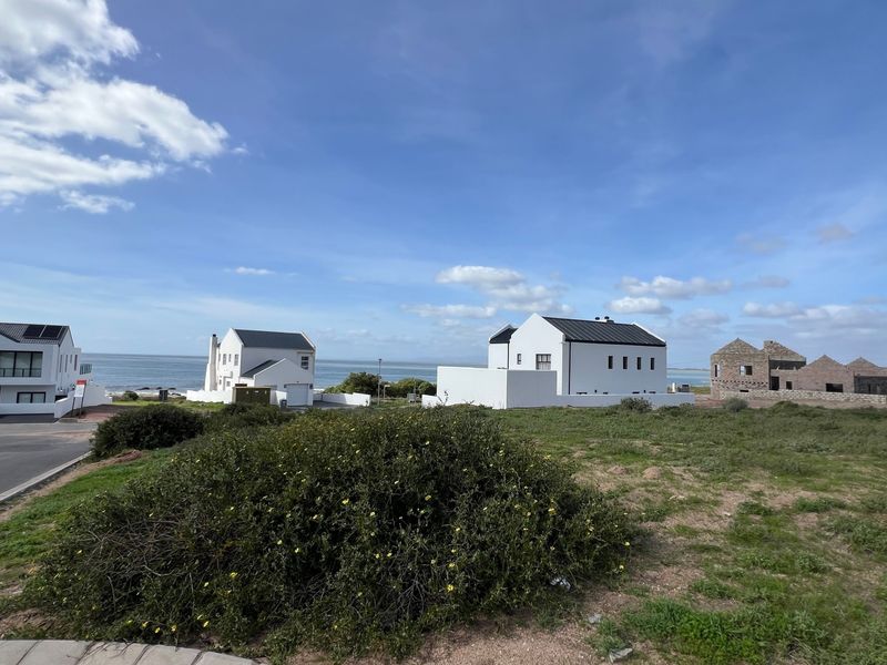 A wide-angle view of a coastal residential area featuring established homes and vacant land under a clear blue sky.