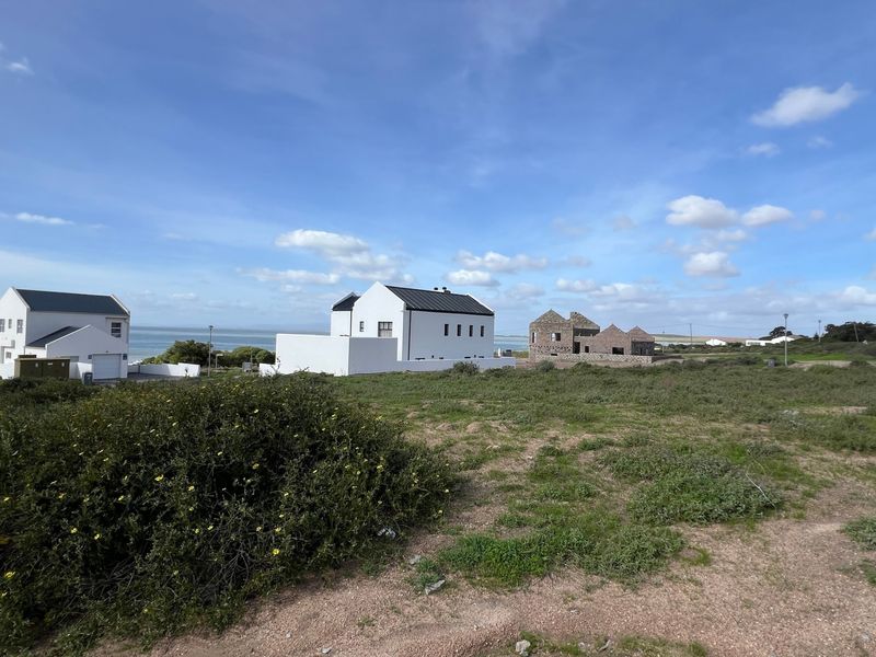 A wide-angle view of a coastal residential area featuring open land, native vegetation, and neighboring properties with ocean views.