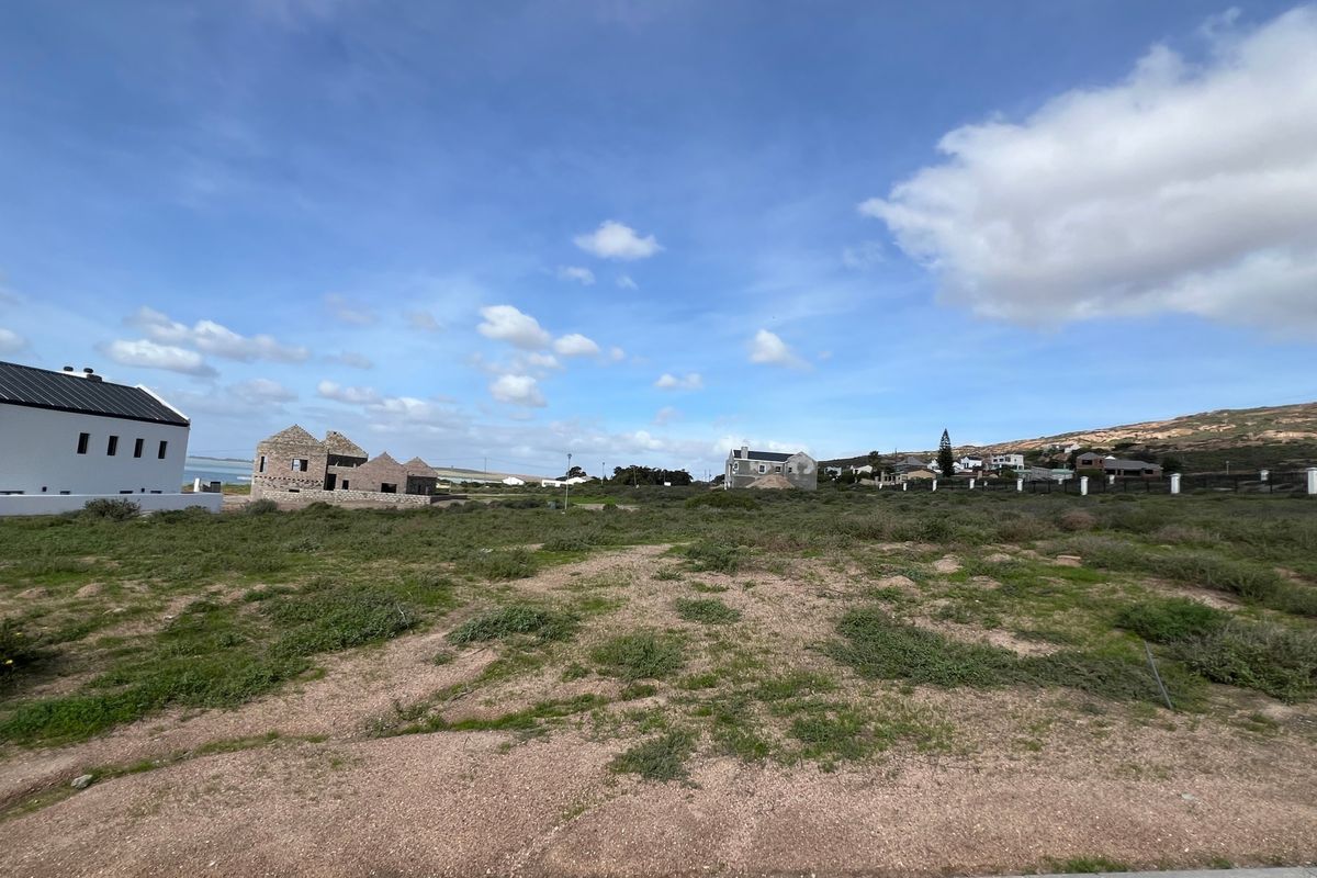 A wide-angle view of a vacant residential plot in a developing coastal neighborhood, featuring natural vegetation and surrounding residential construction.