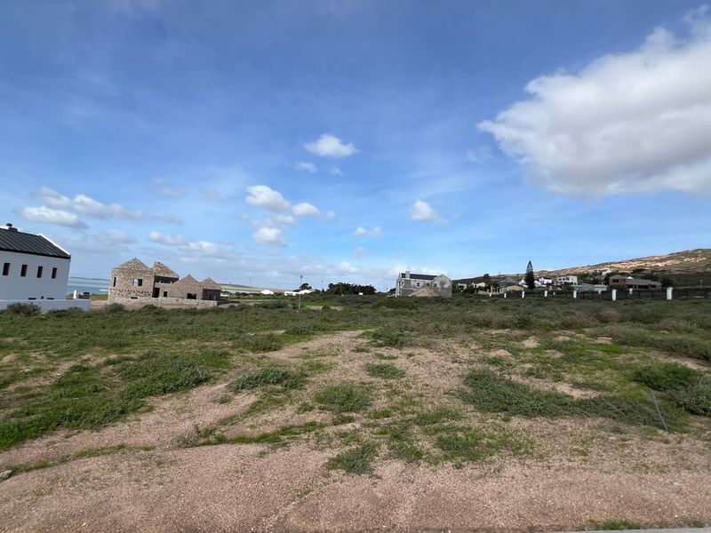 A wide-angle view of a vacant residential plot in a developing coastal neighborhood, featuring natural vegetation and surrounding residential construction.
