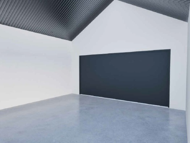A clean, modern, and spacious empty garage featuring polished concrete floors, high vaulted ceilings, and a large dark-toned garage door.