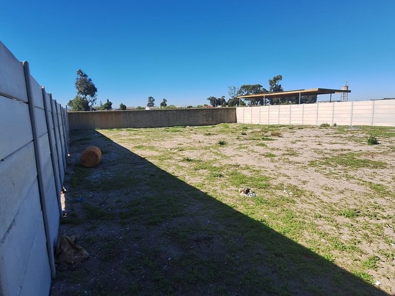 A vacant residential plot enclosed by precast concrete boundary walls, featuring level ground with sparse vegetation.