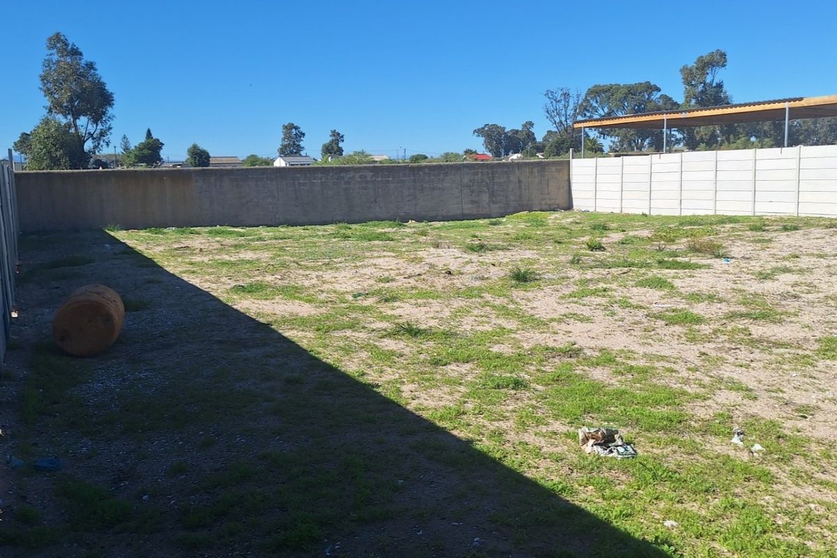 A vacant residential plot enclosed by precast concrete boundary walls, featuring a basic carport structure at the rear.