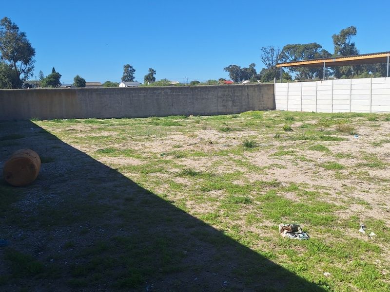 A vacant residential plot enclosed by precast concrete boundary walls, featuring a basic carport structure at the rear.