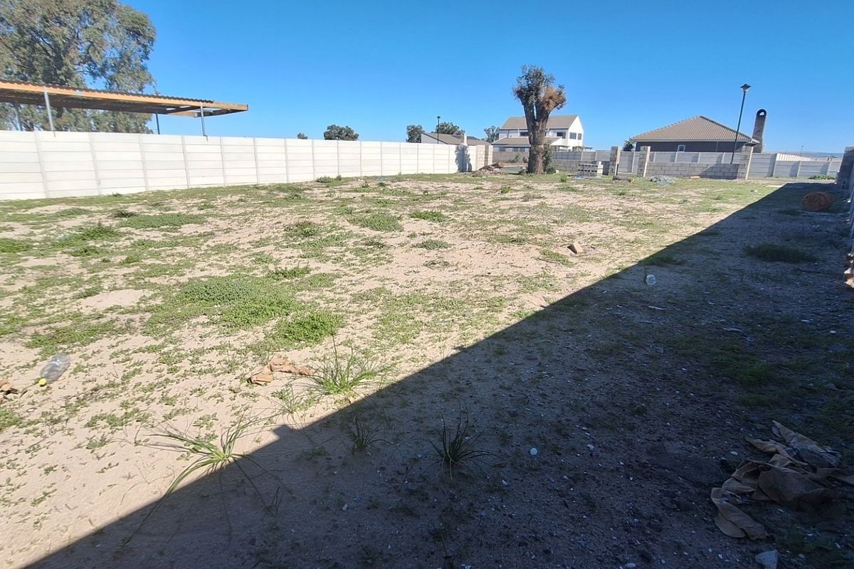 A vacant residential plot enclosed by precast concrete boundary walls, featuring an existing carport structure and undeveloped ground.