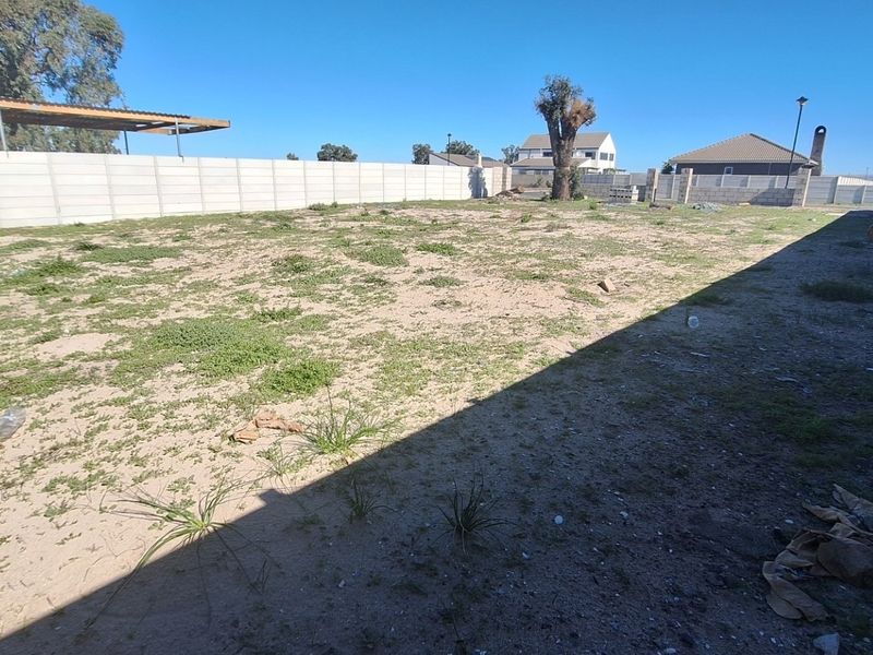 A vacant residential plot enclosed by precast concrete boundary walls, featuring an existing carport structure and undeveloped ground.