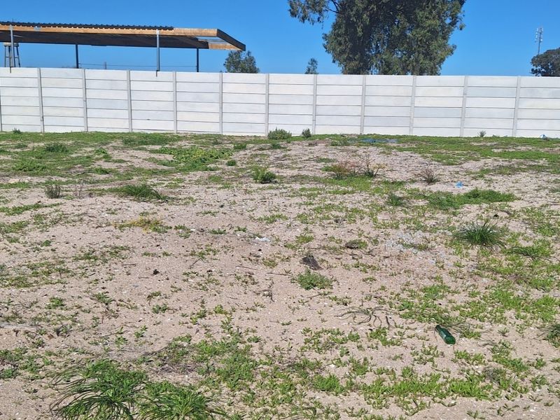 A vacant residential plot featuring a precast concrete boundary wall and a basic covered outdoor structure.