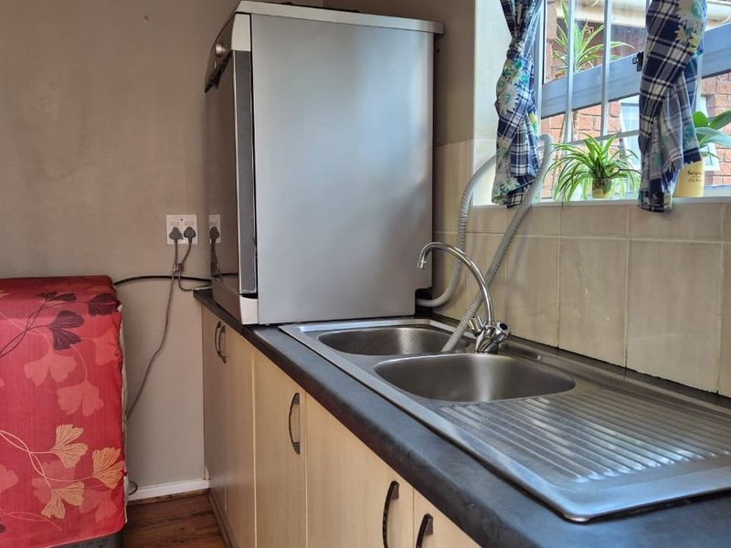 Functional laundry area featuring a double bowl stainless steel sink, laminate cabinetry, and tiled splashback with window security bars.