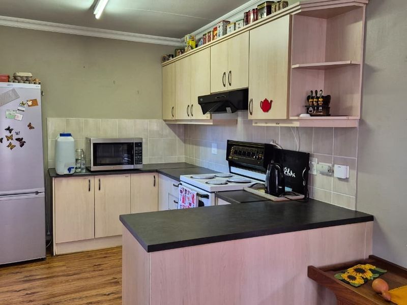 A functional kitchen featuring light-toned laminate cabinetry, dark countertops, a tiled backsplash, and an integrated electric stove with an extractor fan.